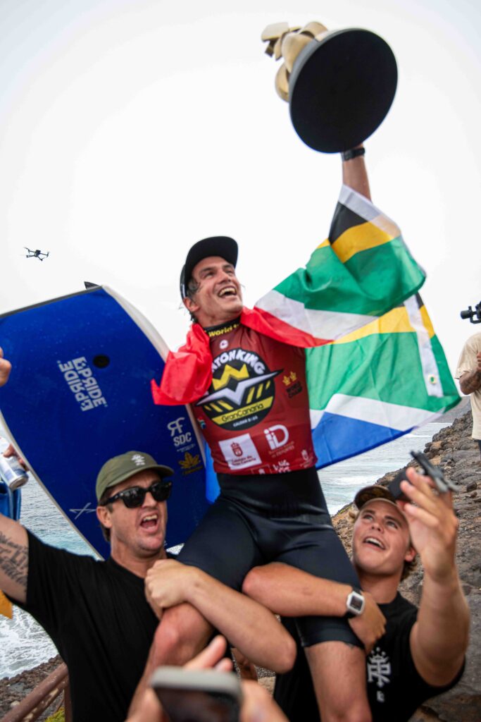 Tristan Roberts, a hombros con el trofeo y la bandera de Sudáfrica tras proclamarse campeón del mundo en El Frontón (Gáldar)